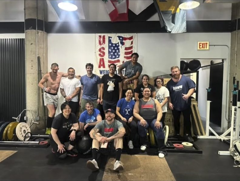 Lifters from the first RAWW Barbell class at Windy City posing on the platforms under the USA Weightlifting banner
