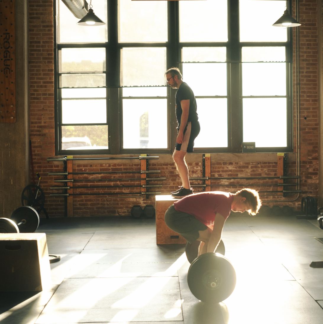 Members deadlifting and doing box step-ups in the afternoon sun from the gym's warehouse windows